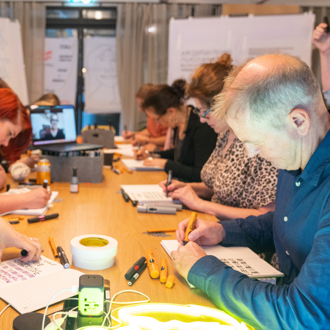 Image of team working together around a table in meeting room using pens and paper 