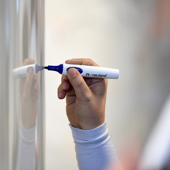Person using Neuland whiteboard marker pen, blue in right hand against whiteboard on wall