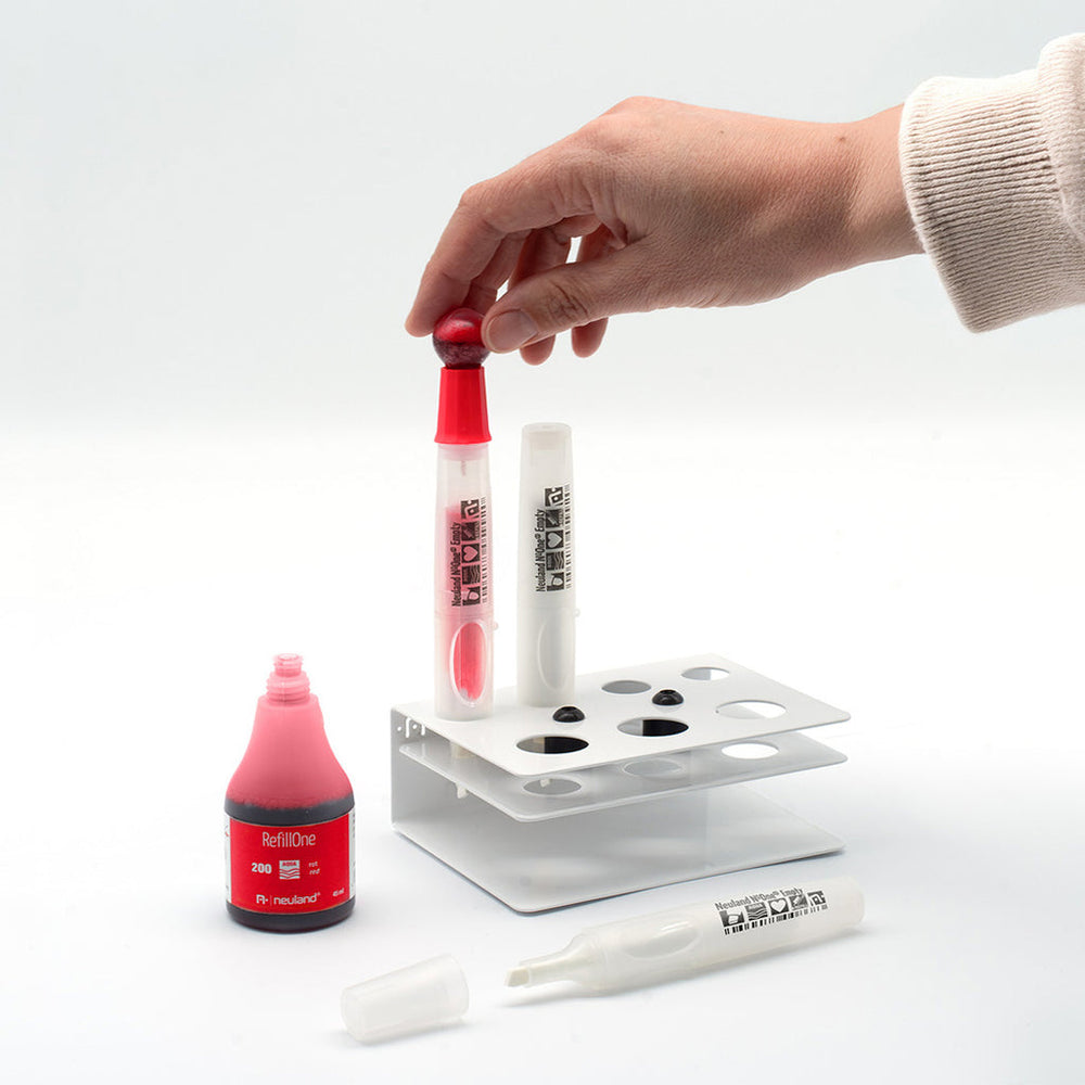 Photo showing empty neuland marker pen being refilled with red ink at refill station. 