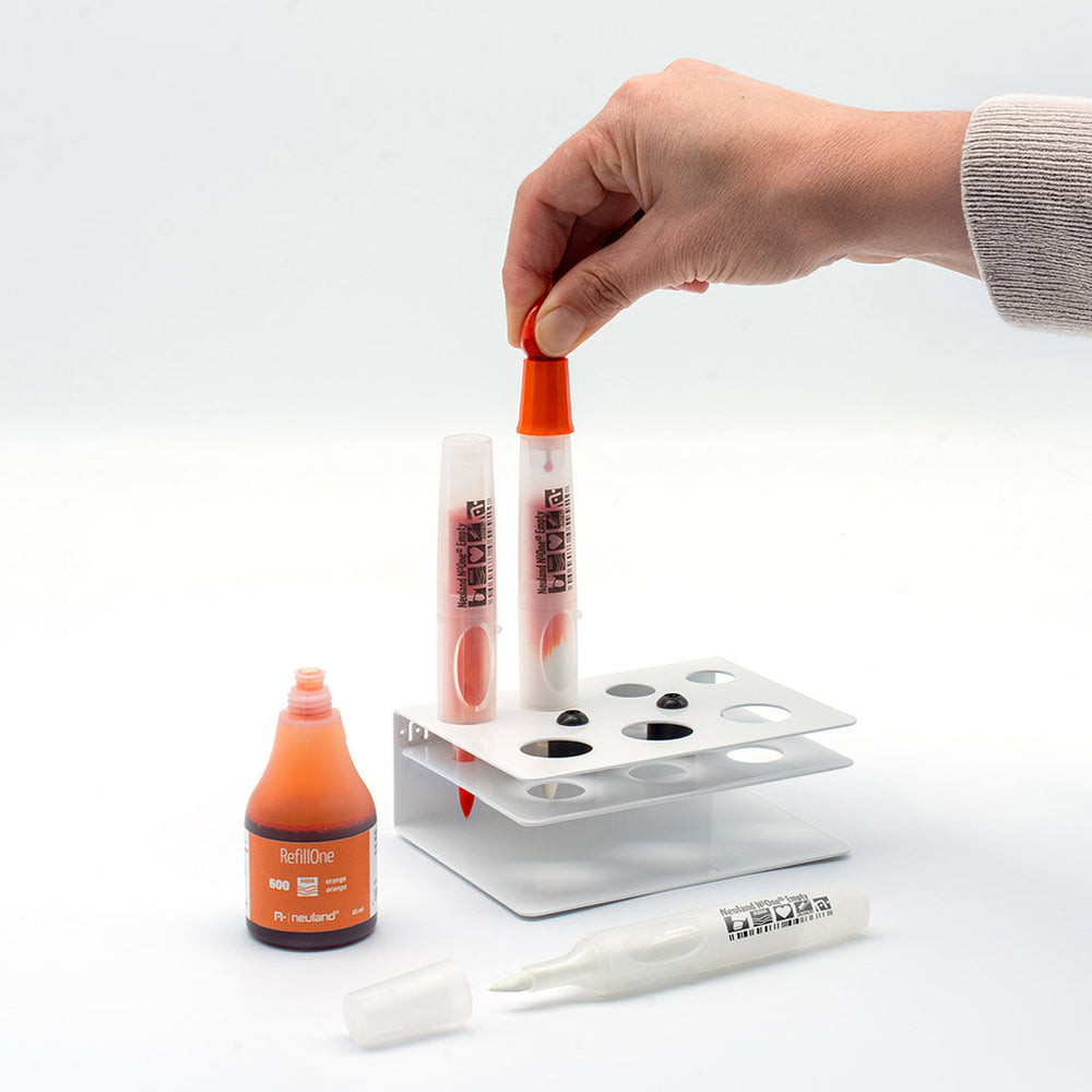 Photo showing neuland marker pen being refilled with orange ink at refill station. 