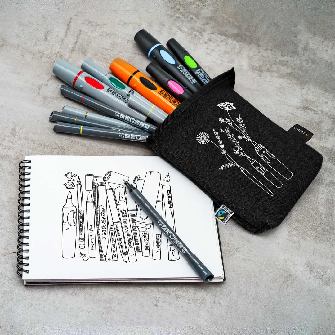 Set of Neuland markers, a pen on a pad, and a black PocketOne pouch with white designs on a grey table surface. Made by Neuland with Fairtrade logo.