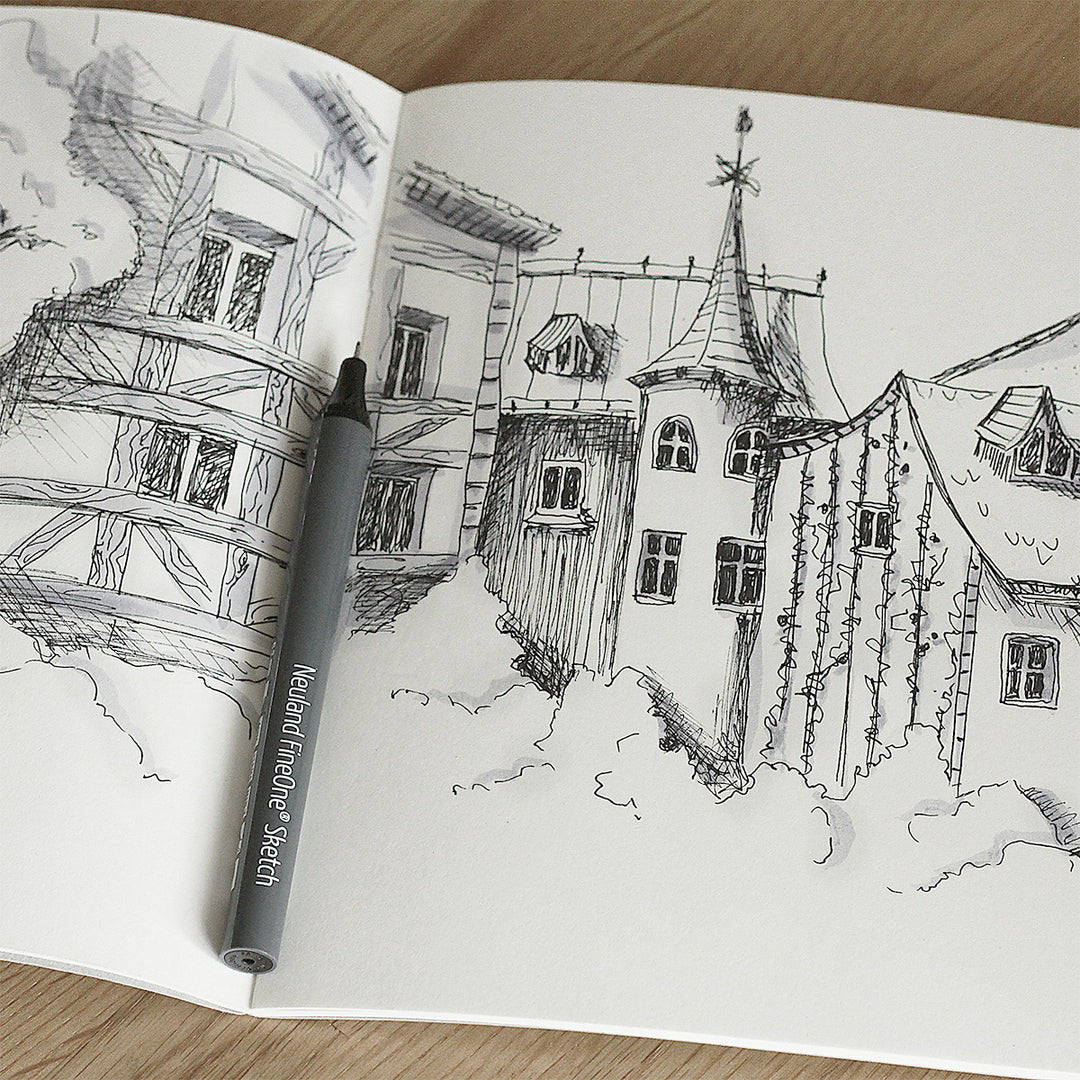 Open Neuland notebook with a black and white drawing of a village scene on a wooden surface using FineOne Sketch pens.