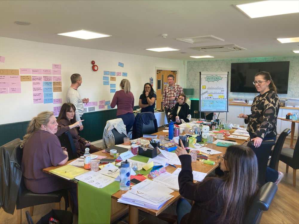 Group of people in a meeting room with tables, chairs, and Estatics statically charged sheets / posters on the walls.