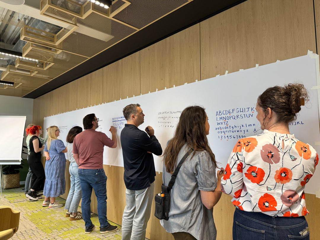 Group of people working on a large whiteboard in a modern office setting with Heather Martinez in collab with Inky Thinking