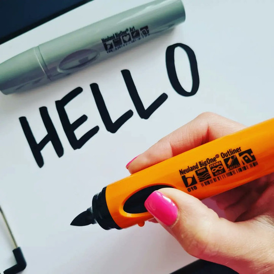 Hand holding Neuland BigOne Art Brush outliner marker, deep black, refillable ink, writing the word 'hello'