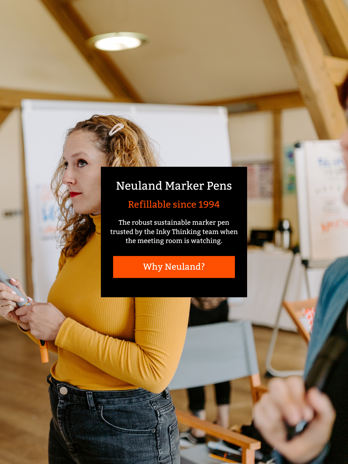 A woman standing in a meeting room at a flipchart holding a refillable Neuland marker pen, with a large black promotional text box overlaid in the centre reading 'Neuland Marker Pens' and supporting copy. 